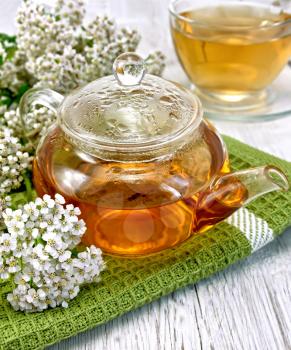 Yarrow tea in a glass teapot on a green napkin, fresh yarrow flowers on a background of light board