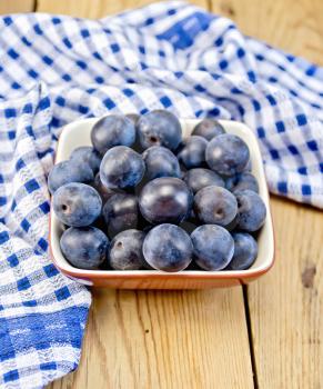 Plum in the blue clay bowl with a blue cloth on a wooden boards background