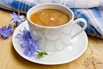 Chicory drink in a white cup with a flower napkin on a wooden boards background