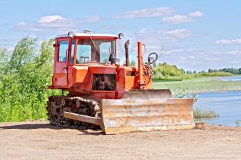 Old red tractor bulldozer on a background of the river of grass and sky