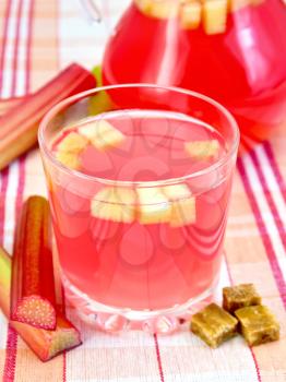 Compote from rhubarb in glassful and pitcher, rhubarb stalks, sugar on linen tablecloth background