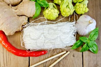 Thin rice noodles, garlic, hot red pepper, ginger, basil and broccoli chopsticks on a wooden boards background
