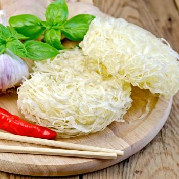 Stranded rice noodles with garlic, red pepper, ginger and basil, chopsticks on a wooden boards background