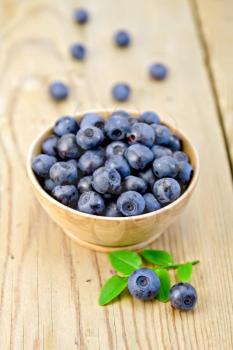 Blueberries in a wooden bowl, twig with green leaves and berries on a wooden boards background