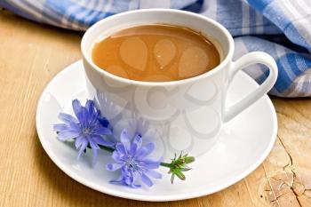 Chicory drink in a white cup with flower, blue cloth on a wooden boards background