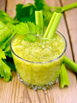 One glassful with a cocktail of celery and two petioles, stems and leaves of celery on a wooden boards background