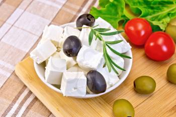 White brine cheese, olives, rosemary in a white bowl, tomatoes, lettuce, olives on a wooden boards background and fabrics