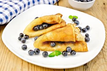 Two pancakes with blueberries, mint on a white plate, napkin, bowl on a wooden boards background