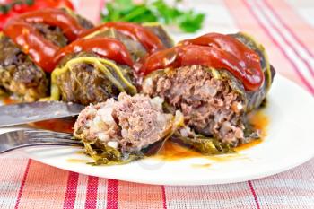 Cabbage rolls with minced meat in the leaves of rhubarb in a plate with tomato sauce, fork, knife on linen background