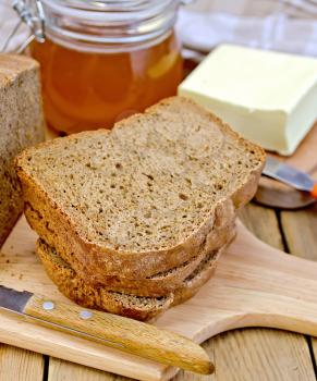A stack of slices of rye homemade bread with a knife, napkin, a jar of honey, butter on a wooden boards background