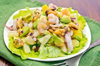 Salad with shrimps, octopus, mussels and calamari with avocado, lettuce, pineapple in a plate on a napkin, fork on the background dark wooden boards