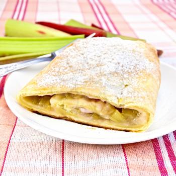 Strudel with rhubarb in a plate, stalks of rhubarb against the background of a linen tablecloth