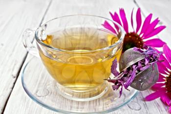 Herbal tea in a glass cup, metal sieve with dry flowers of Echinacea, Echinacea fresh flowers on the background light wooden boards