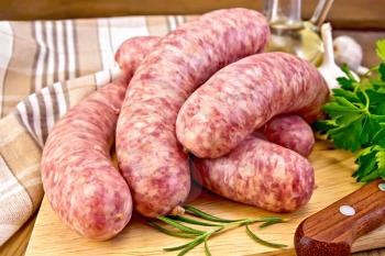 Raw pork sausages, knife, rosemary, parsley, vegetable oil, garlic and napkin on a wooden boards background