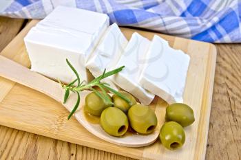 White brine cheese, rosemary, olive in spoon, blue plaid napkin on a wooden boards background