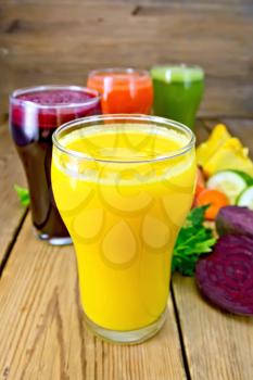 Four tall glass of carrot juice, cucumber, beetroot and pumpkin, vegetables, parsley on a wooden boards background
