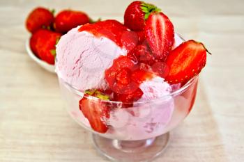 Strawberry ice cream in a glass bowl with strawberries on a fabric background