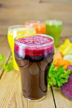 Beet juice in the foreground and carrot juice, pumpkin and cucumber in a tall glass, vegetables on a wooden boards background