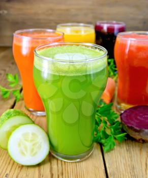 Five tall glasses with the juice of carrot, cucumber, beetroot, tomato and pumpkin with vegetables, parsley on a wooden boards background