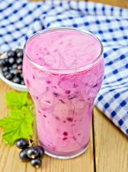 Milkshake with black currants in a tall glass beaker, blue cloth, currant berries on a wooden boards background
