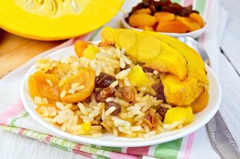 Pilaf fruit with pumpkin, raisins, dried apricots in a white plate on a napkin, pumpkin, dried fruits, spoon background of light wooden boards