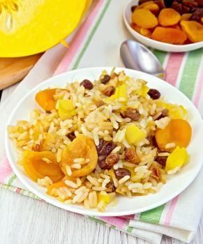 Pilaf fruit with pumpkin, raisins, dried apricots in a white plate on a napkin, pumpkin, dried fruits, spoon on a wooden boards background