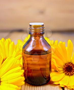 Dark bottle of aromatic oil, yellow marigold flowers on a background of wooden planks