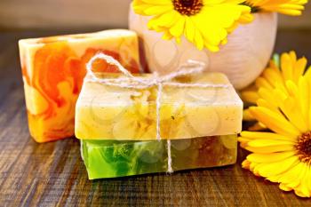 Homemade soap, a wooden mortar, yellow marigold on a wooden boards background