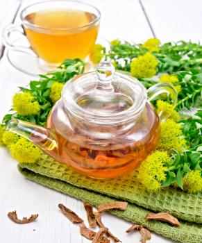 Herbal tea in a glass teapot from the root of Rhodiola rosea on a napkin, cup, fresh flowers Rhodiola rosea on the background light wooden boards