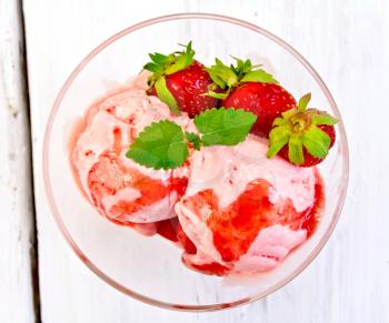 Strawberry ice cream in a glass with strawberries, mint and strawberry syrup on the background light wooden boards on top