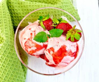 Strawberry ice cream in a glass with strawberries, mint and strawberry syrup, napkin on the background light wooden boards on top