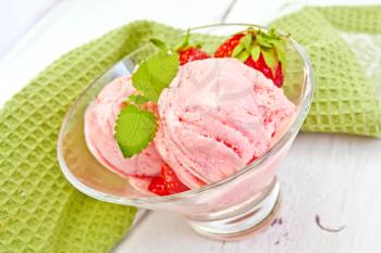 Strawberry ice cream in a glass with strawberries and mint, napkin on the background light wooden boards
