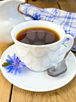 Chicory drink in a white cup with a flower on a saucer and spoon, napkin, milkman with milk on a wooden boards background