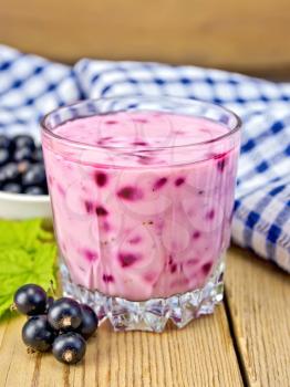 Milkshake with black currants in a low glass beaker, napkin, currant berries on a wooden boards background