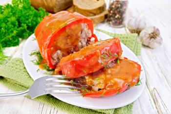 Sweet pepper stuffed with meat and rice with tomato sauce on a plate on a napkin, fork, dill, parsley on the background light wooden boards