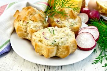 Appetizer of radish, dill, eggs and cheese in profiteroles on a white plate, napkin on the background light wooden boards