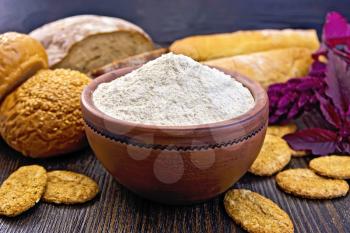 Amaranth flour in a clay bowl with bread and biscuits, purple amaranth flower on the background of wooden boards