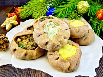 Carols of rye flour filled with cheese, potatoes and mushrooms on paper, Christmas decorations, fir branches on the background of wooden boards