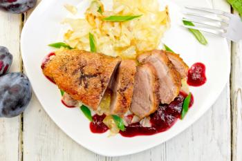 Roasted duck breast with braised cabbage, green onions and plum sauce in white plate, plums on a background of light wooden boards on top