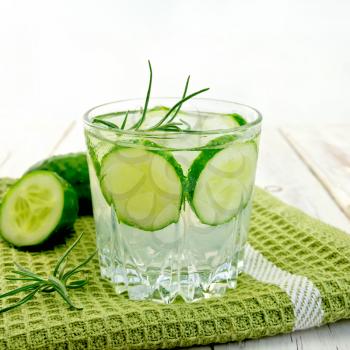 Lemonade with a cucumber and rosemary in a glass on a green napkin on a wooden boards background