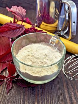 Amaranth flour in a glass cup, mixer, rolling pin and sieve, purple amaranth flower on the background of wooden boards