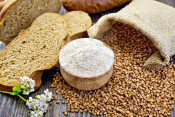 Buckwheat flour in a wooden bowl, buckwheat in the bag, slices of bread, buckwheat flower on the background of wooden boards