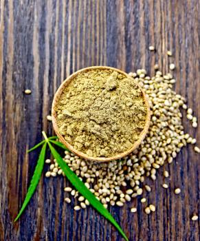 Hemp flour in a bowl, corn and green leaves of hemp on a background of wooden planks on top