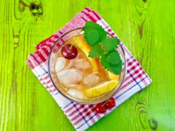 Lemonade in a glass with a cherry, lemon and orange, mint on a napkin on a green wooden boards on top