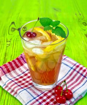 Lemonade in a glass with a cherry, lemon and orange, mint on a napkin on a green wooden board