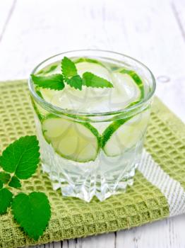 Lemonade with cucumber and mint in a glass on a green napkin on the background light wooden boards
