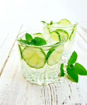 Lemonade with cucumber and mint in two glassful, sliced cucumber on a light wooden boards background