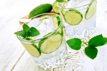 Lemonade with cucumber and mint in two glasses, a knife, a cucumber on a white background wooden board