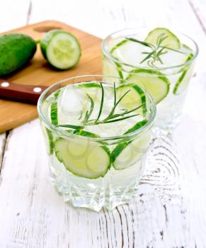 Lemonade with a cucumber and rosemary in two glassful, a knife, a cucumber on a wooden boards background