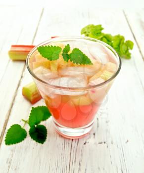 Lemonade with rhubarb and mint in a glass, the stems and leaves of rhubarb on the background light wooden boards